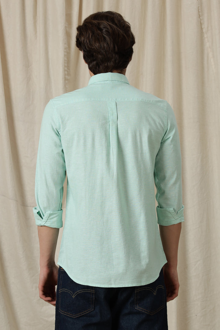 Person wearing a light green shirt with rolled-up sleeves against a beige curtain background
