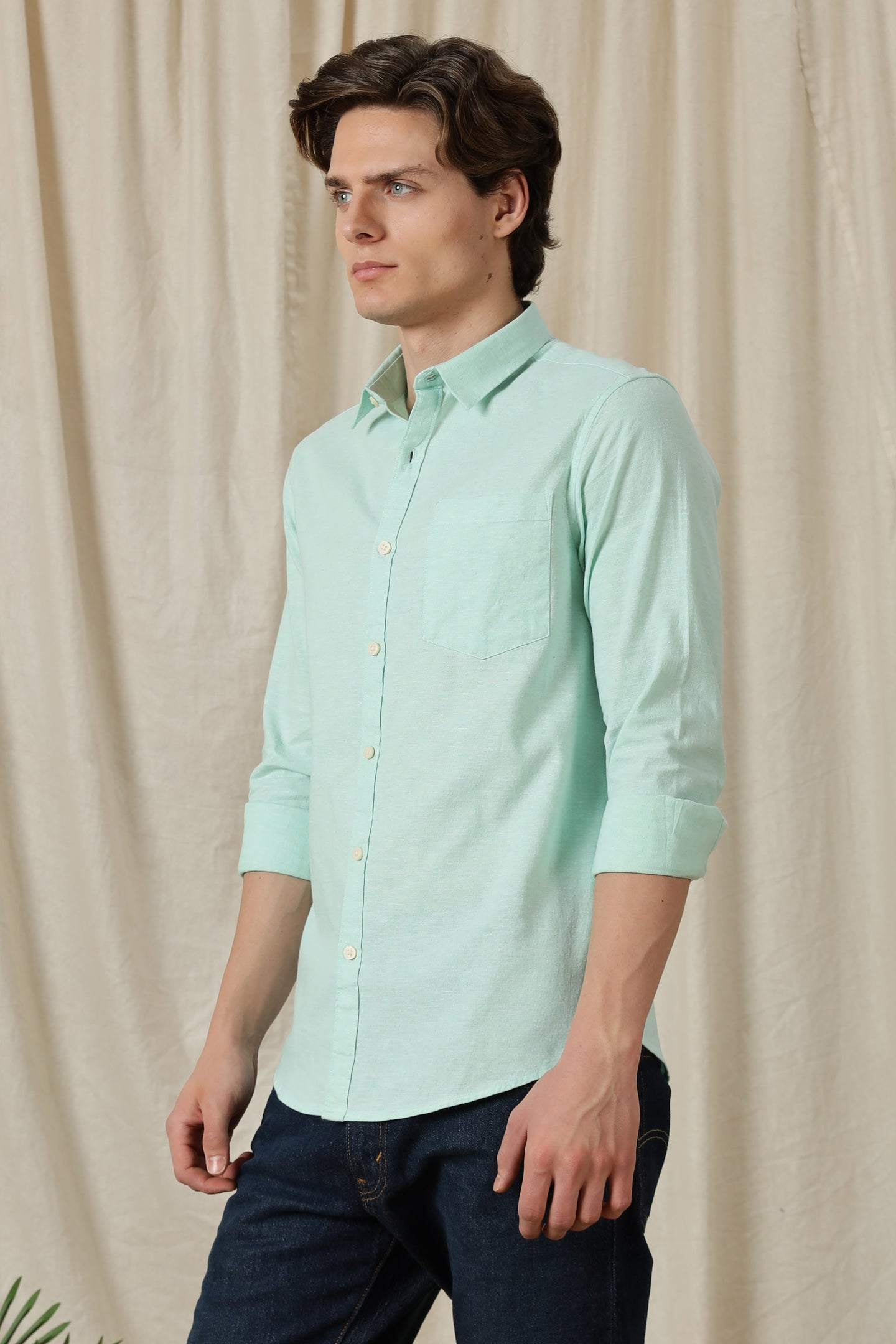 Man wearing a light green shirt against a beige curtain background