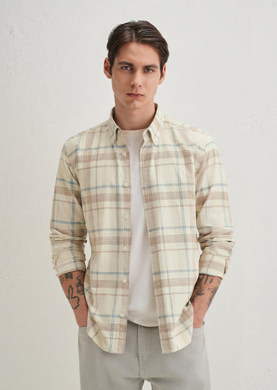 Man wearing a plaid shirt over a plain shirt on a light background